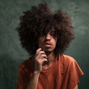 Man met zwarte afro kijkt in de camera met zijn haar half voor zijn ogen